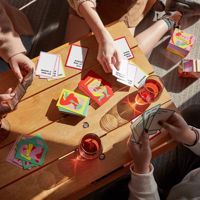 image vue de haut, plusieurs mains jouent aux cartes et boivent des verres autour d'une table