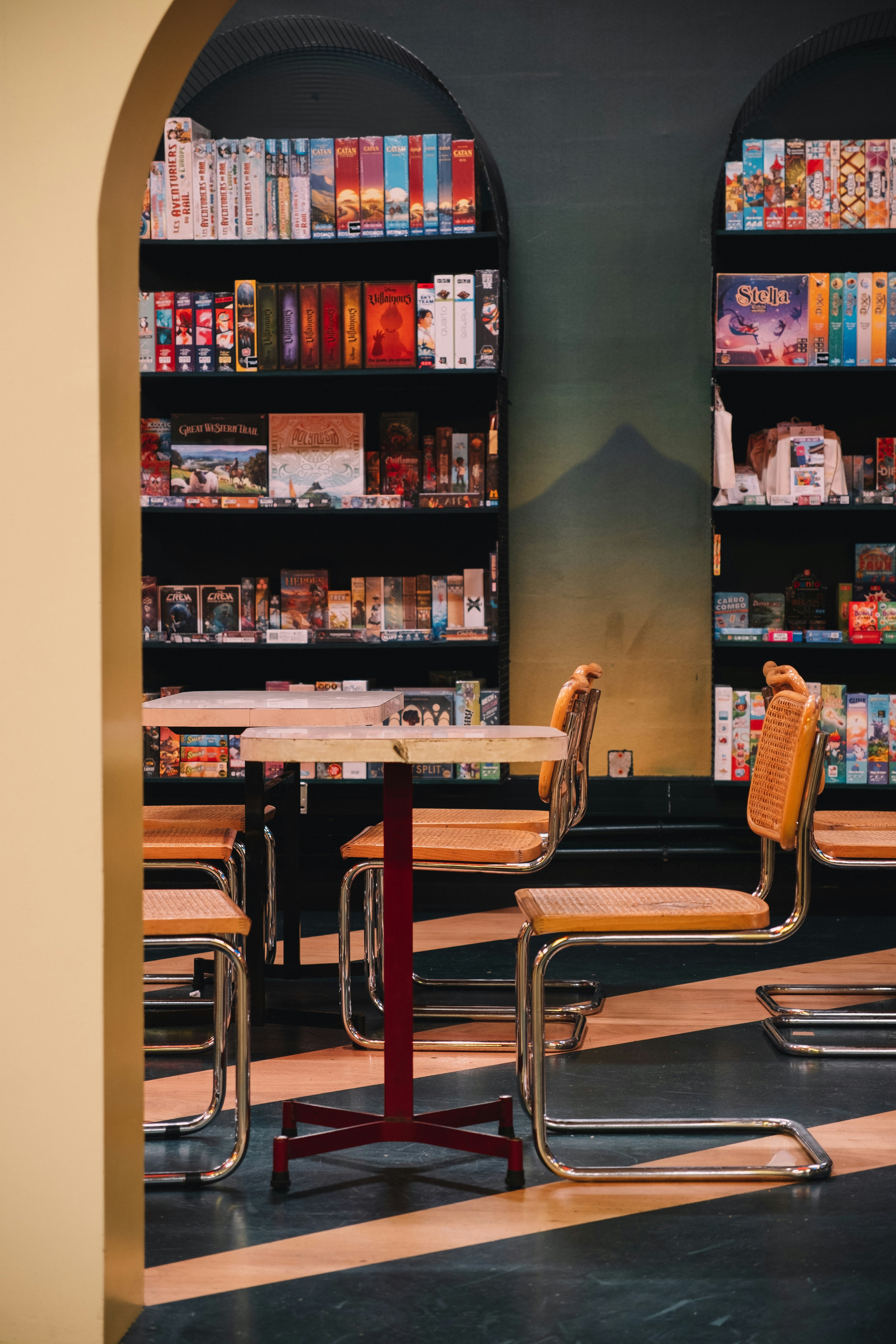 vu de profil d'une salle ou d'un bar à jeux de société, avec tables et chaises, au fond des étagères remplies de jeux de société